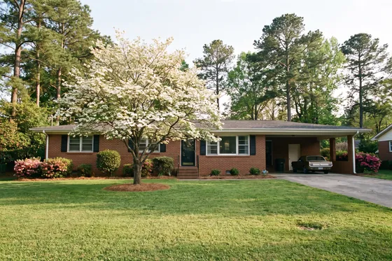A 1960s brick ranch house with a low roofline and a dogwood tree in the front lawn